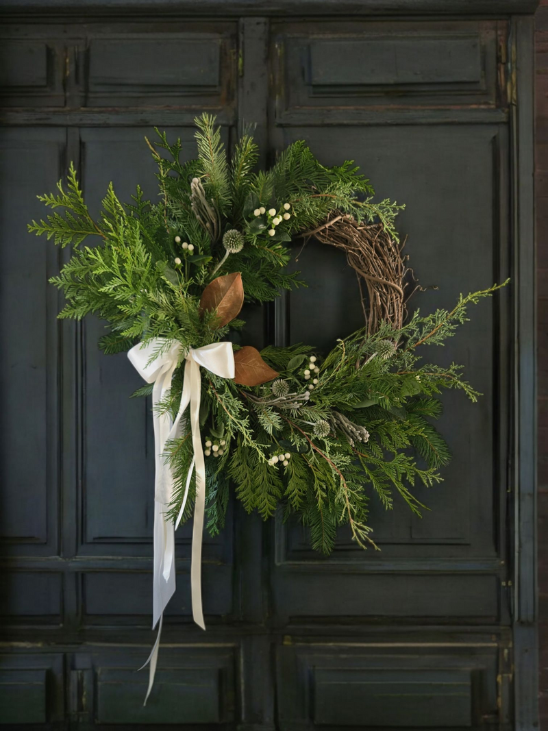 Green wreath with a white ribbon on a dark wooden door