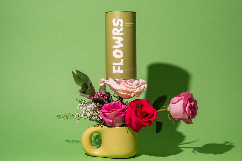 Floral arrangement in a green vase with a 'FLOWRS' canister on a green background