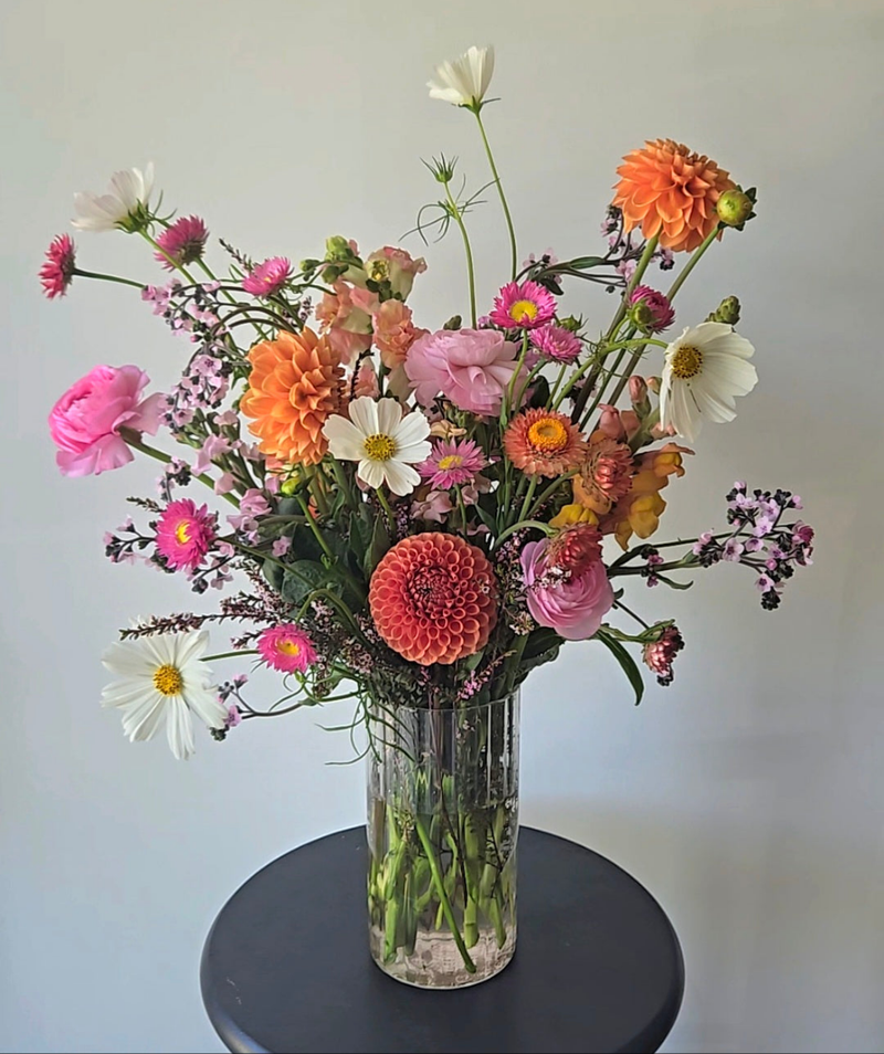 Bouquet of colorful flowers in a clear vase on a dark surface with a light background