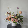 Floral arrangement in a white container on a dark surface with a light gray background