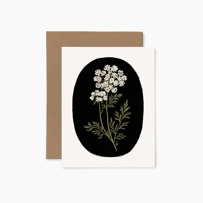 A black greeting card with a colorful illustration of a plant with white flowers, accompanied by a brown envelope.