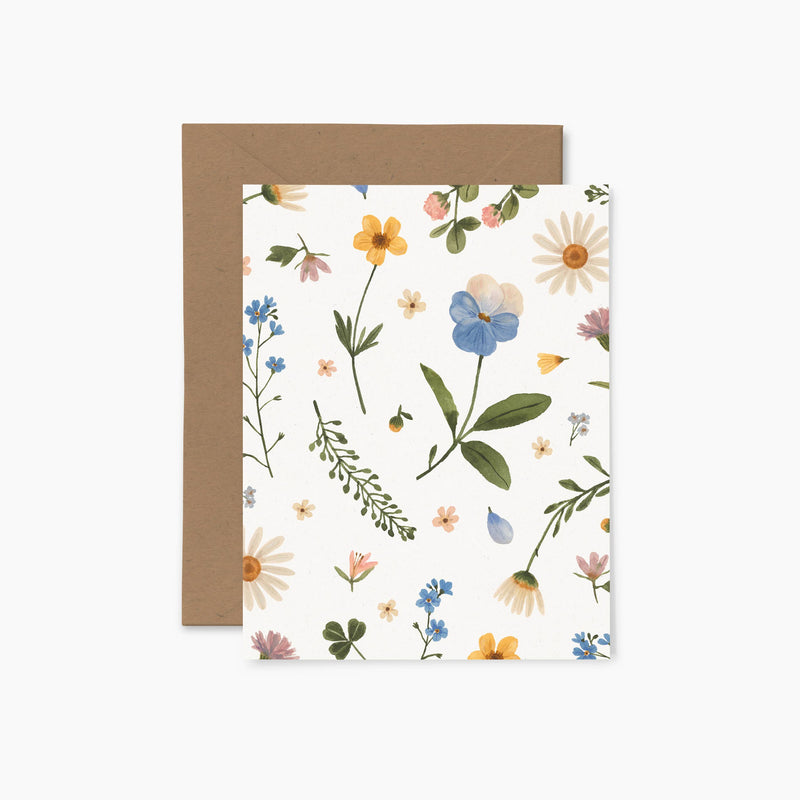 A folded greeting card with a floral pressed flower pattern, accompanied by a brown envelope.
